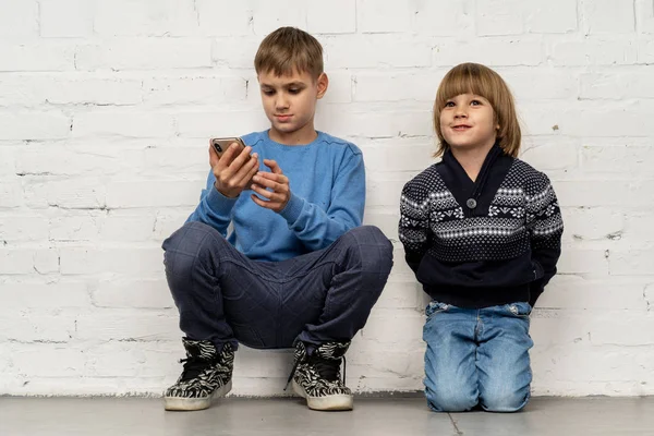 Two serious children sitting on floor against white wall in children room