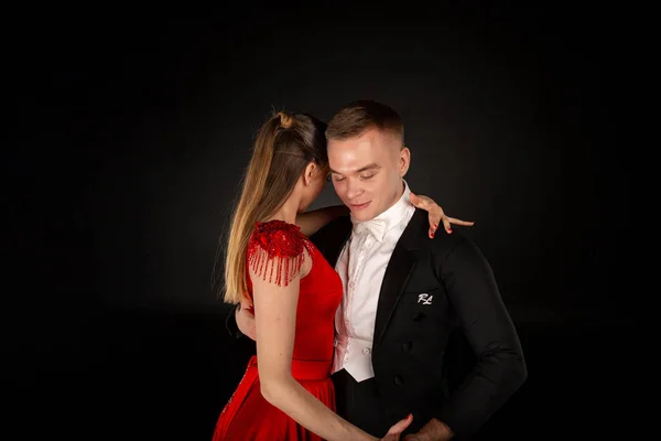 Bonita joven vestida de rojo bailando tango con hombre en traje negro — Foto de Stock