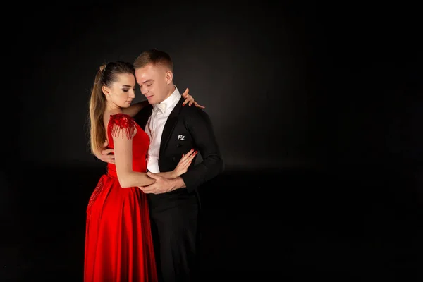 Bonita joven vestida de rojo bailando tango con hombre en traje negro — Foto de Stock