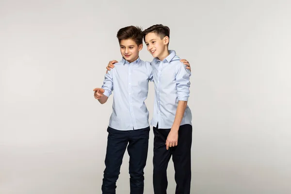 Portrait of two young brothers in blue shirts with short hair, one is pointing right, showing somesing to his brother