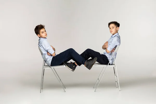 Allvarlig bröder tonåringar sitter på stolar mot varandra — Stockfoto