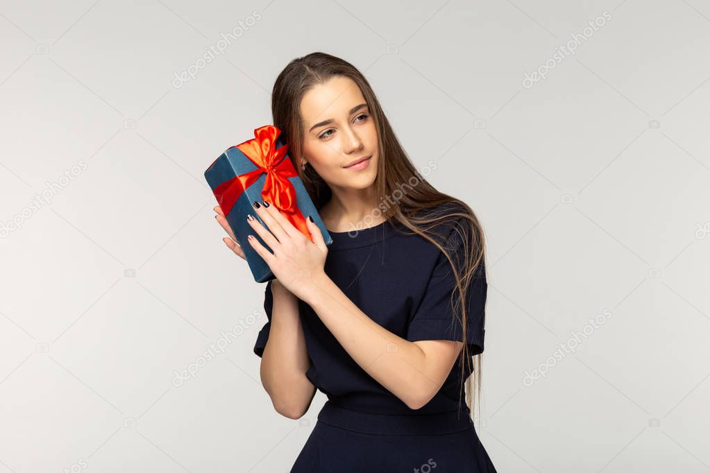 A beautiful young girl with brown hair and natural makeup holding a black gift box with a red ribbon