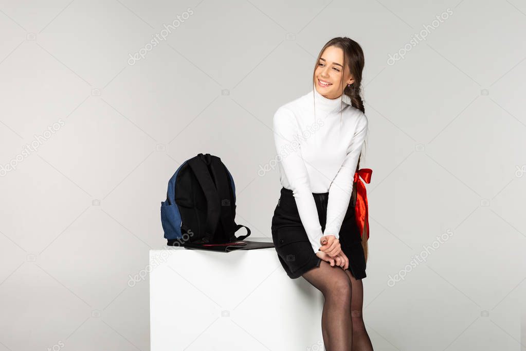 Beautiful smiling schoolgirl in white golf with long braid and red bow