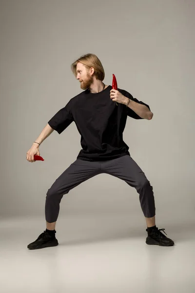 Young karate master in black wear posing with two red chilli peppers in hands — Stock Photo, Image