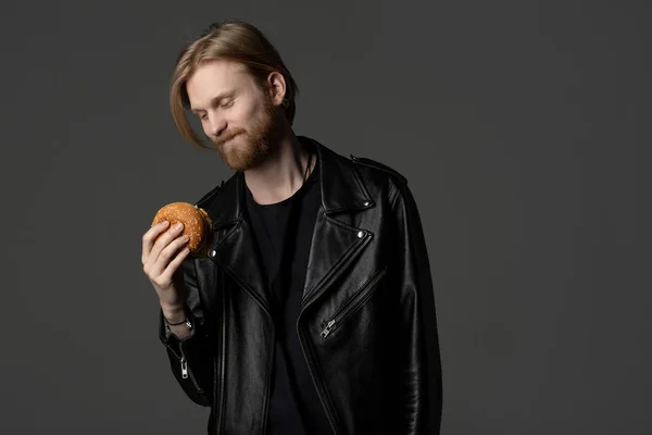 Aantrekkelijke man met baard en lange haren kijken naar burger in zijn hand — Stockfoto