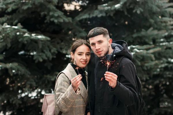 Romantic young couple is having fun outdoors in winter before Christmas with bengal lights — Stock Photo, Image