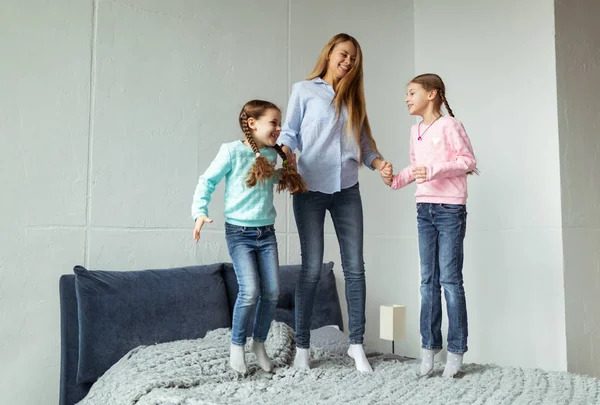 Lycklig familj mamma och två daghters hoppar på sängen — Stockfoto