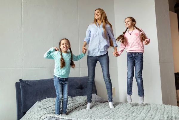 Lycklig familj mamma och två daghters hoppar på sängen — Stockfoto