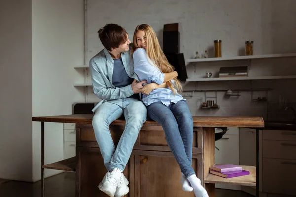 Feliz sorrindo jovem casal em pano de ganga azul sentado na cozinha — Fotografia de Stock