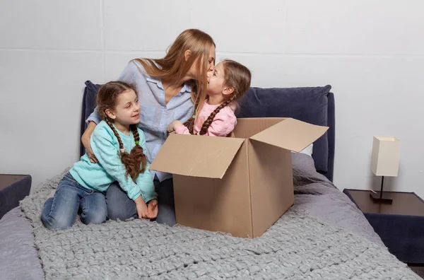 Lycklig familj, ung mamma med två döttrar sitter på sängen i nytt hem — Stockfoto