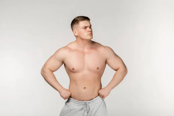 Young hamdsome bodybuilder posing in the studio, holds hands on waist — 图库照片