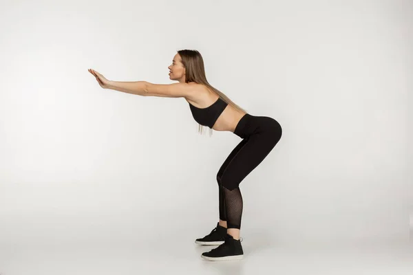 Вид сбоку фото молодой красивой женщины в черной спортивной одежде делает упражнения приседания — стоковое фото