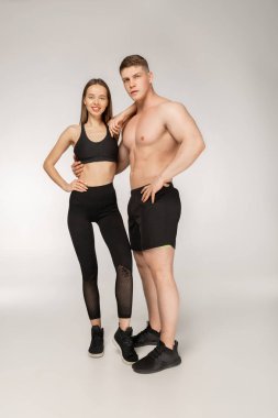 Gömleksiz atletik erkek ve genç kadın siyah spor giyim üzerine poz içinde arka plan gri