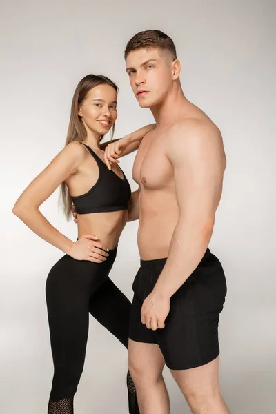 Спортивний чоловік без сорочки і молода жінка в чорному спортивному одязі позує на сірому фоні — стокове фото
