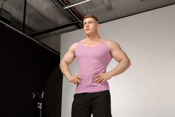 Muskulöser junger Mann in rosa T-Shirt posiert mit den Händen am Gürtel — Stockfoto