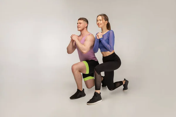 Pasangan muda yang sporty dalam trendi berwarna-warni pakaian olahraga melakukan lunge pada kaki kiri — Stok Foto