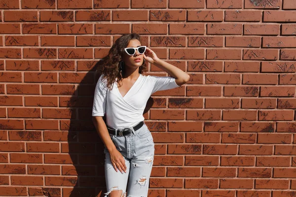 Attarctive elegante jovem hipster com óculos de sol brancos em calças jeans de verão e camiseta branca — Fotografia de Stock