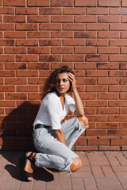 Beyaz t-shirt ve kot pantolon içinde açık kahverengi kıvırcık saçlı genç muhteşem kız