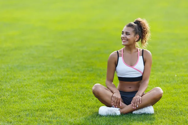 Young happy girl with curly hair in sportswear sitting in the lotus position — Stock Photo, Image