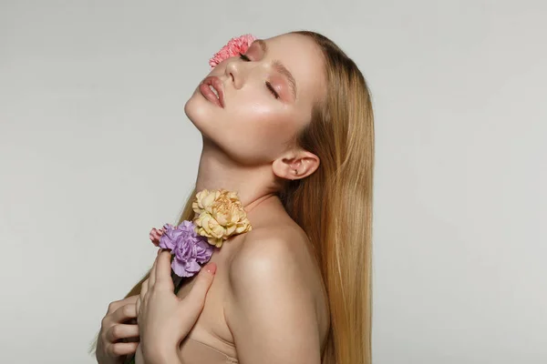 Visão lateral retrato de encantadora jovem loira com maquiagem perfeita e olhos fechados, flores prensadas para seu corpo — Fotografia de Stock