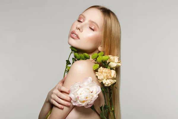 Vue de côté portrait de charmante jeune fille blonde avec un maquillage parfait et les yeux fermés, pressé des fleurs à son corps — Photo