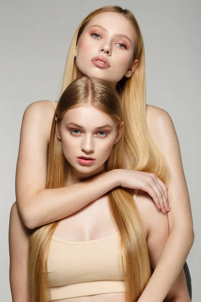 Dos hermosas hermanas gemelas con el mismo pelo largo rubio y la piel perfecta — Foto de Stock