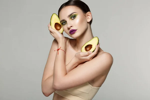 Portrait de beauté d'une jolie femme en bonne santé avec un avocat frais tranché dans les mains croisées près du visage — Photo