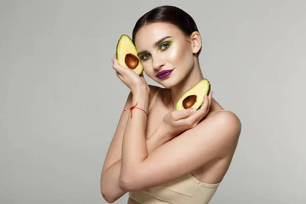 Portret van de schoonheid van een aantrekkelijke gezonde vrouw met gesneden verse avocado in gekruiste handen in de buurt van gezicht — Stockfoto