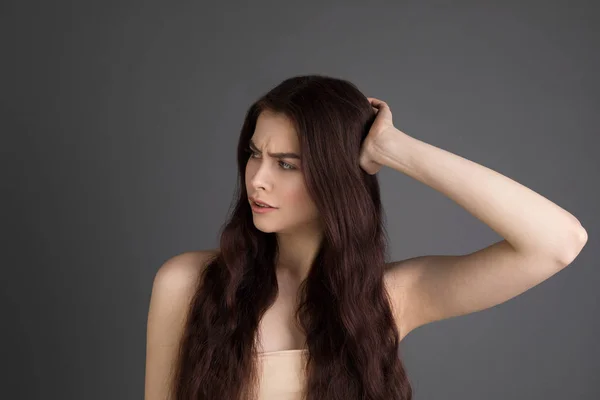 Портрет недовольной юной брюнетки, касающейся волос — стоковое фото