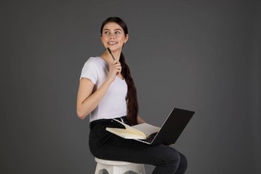 Beyaz t-shirt mutlu esmer kız güzel kitap ve dizüstü bilgisayar kullanarak sandalyeye oturur