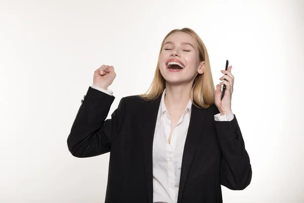 Retrato de la mujer impresionada y atractiva de pelo rubio en traje negro, sosteniendo el teléfono inteligente y haciendo gestos de emoción — Foto de Stock