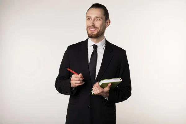 Retrato aislado del hombre barbudo en traje negro y corbata con peinado de moda haciendo notas en su cuaderno — Foto de Stock