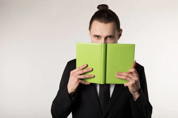 Joven en traje negro con peinado de moda oculta su cara detrás del libro verde — Foto de Stock