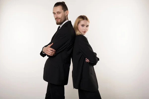 Concepto de asociación en los negocios. Hombre guapo y mujer hermosa, ambos en trajes negros de pie espalda con las manos cruzadas — Foto de Stock