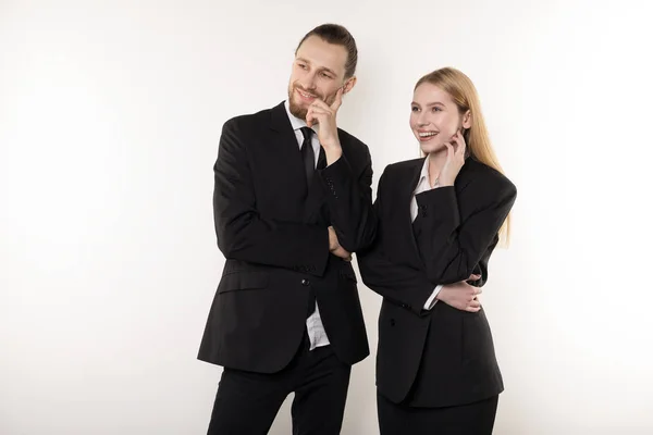 Dos empleados felices en trajes negros de pie junto con las manos en la cintura mirando la presentación de su jefe — Foto de Stock