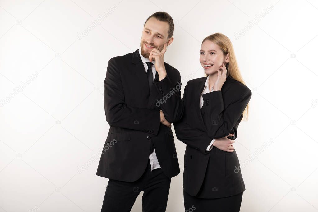 Two happy employees in black suits standing together with hands on waist looking at the presentation of their boss