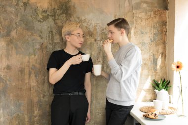 Uluslararası yakışıklı homoseksüel erkekler kahve içiyor ve mutfakta birbirlerine bakıyor. Rahat giysiler, sarışın Asyalı erkekler gözlük ve kahverengi saçlı Avrupa adam giyiyor