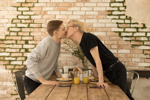 Casal romântico romântico internacional do mesmo sexo beijar uns aos outros em toda a mesa em casa — Fotografia de Stock