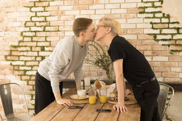 International romantic hot same-sex couple kiss each other across the table at home — Stock Photo, Image