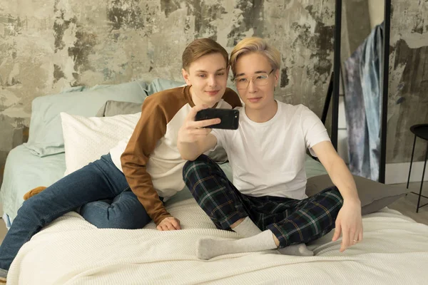 Casal homossexual internacional atraente relaxando na cama antes do sono da noite e olhando para a tela do smartphone — Fotografia de Stock