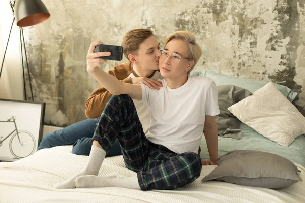 Casal masculino internacional de orientação não-tradional vestida com roupas casuais relaxando juntos na cama — Fotografia de Stock