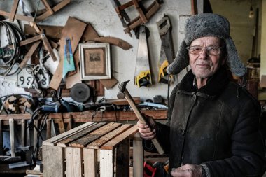 Elinde çekiç ile gri sıcak giysiler ve gözlük çok yaşlı adam Master