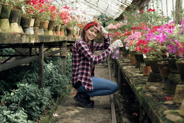 Joven niña feliz jardinero en una camisa a cuadros con una diadema roja regando flores — Foto de Stock
