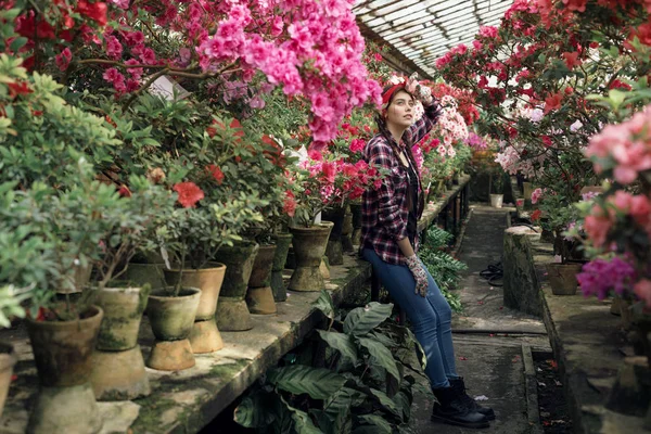 Hermosa joven jardinero con coletas y diadema roja descansando después de un duro trabajo con flores de primavera en invernadero — Foto de Stock