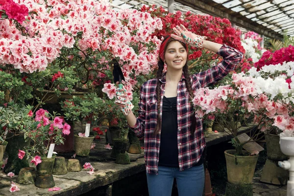 Foto de la joven jardinero feliz en una camisa a cuadros que sostiene la pala pequeña con el patio rosado y rojo en el fondo — Foto de Stock