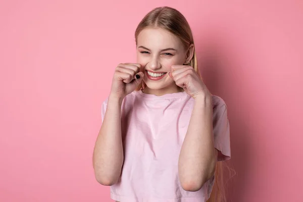 Portrait mi-long de belle fille blonde aux yeux bleus, portant un t-shirt rose, avec les poings près du visage — Photo