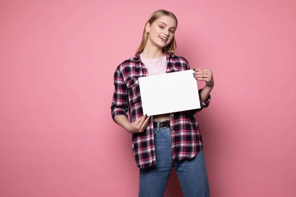 Joyeux sourire jeune femme blonde en vêtements décontractés debout contre le mur rose — Photo