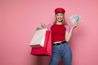 Renkli alışveriş çantaları ve elinde para ile rahat giysiler ve trendy kırmızı şapka Pretty genç kadın