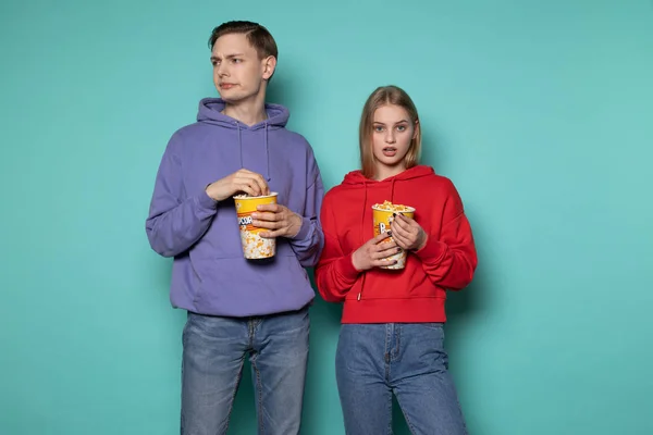 Unga upprörda par i casual kläder titta på motsägelsefull film, hålla hink popcorn — Stockfoto