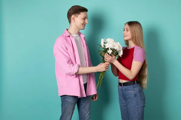 Guapo joven en camisa rosa da un ramo de flores blancas a su hermosa novia rubia — Foto de Stock